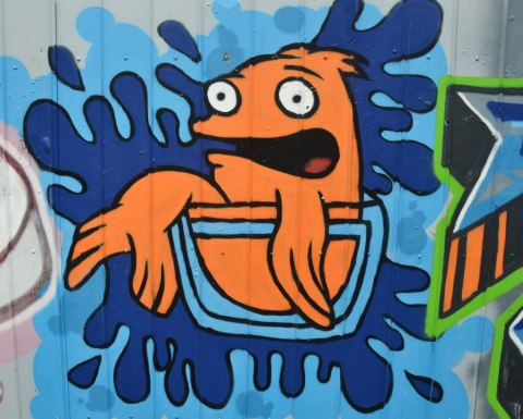 a street art painting of an orange fish (not realistic looking) sitting in a glass bowl, with a surprised expression on its face 