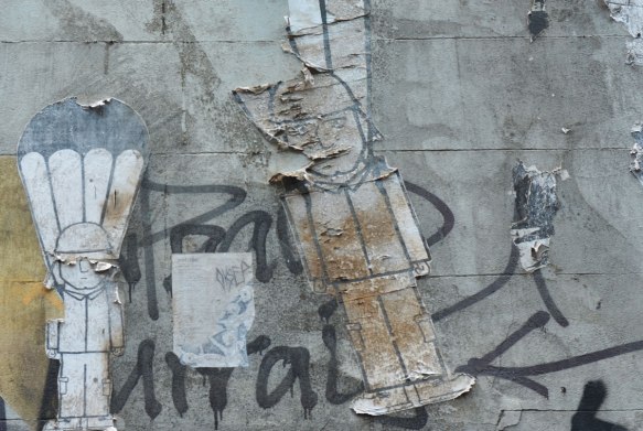 paper wheatpastes on a wall. They are of men with parachute strings behind ad above them. They are peeling. 