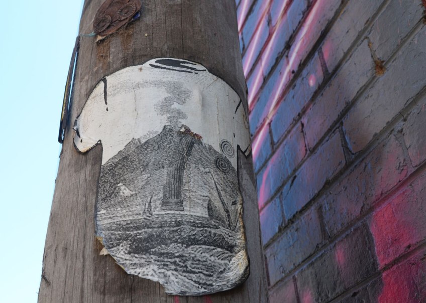 High on a pole, a paste-up of a white T-shirt on which there is a large black and white a detailed bdrawing