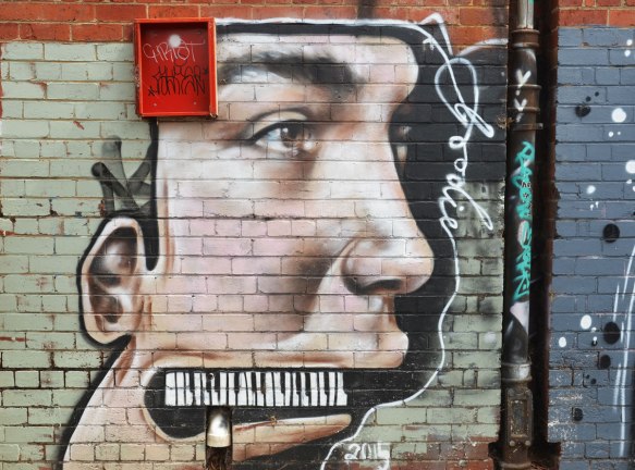 street art painting of a young man's face in profile, instead of teeth he has a piano keyboard