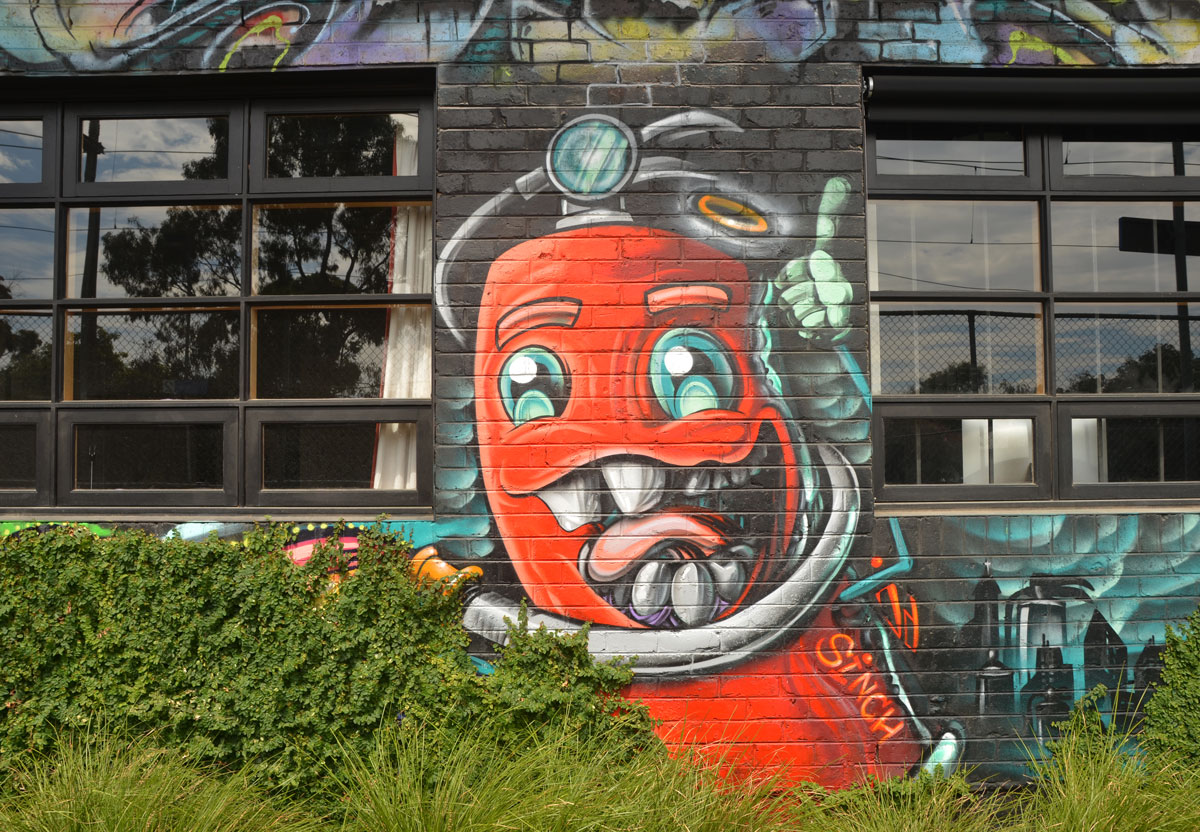 cartoon painting of a red fire hydrant (or maybe fire extinguisher) with a big mouth, several teeth, and a tongue, two eyes, and hoses for arms. 