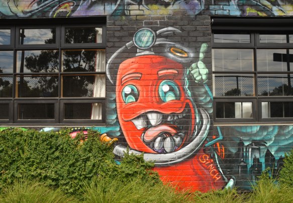 cartoon painting of a red fire hydrant (or maybe fire extinguisher) with a big mouth, several teeth, and a tongue, two eyes, and hoses for arms. 