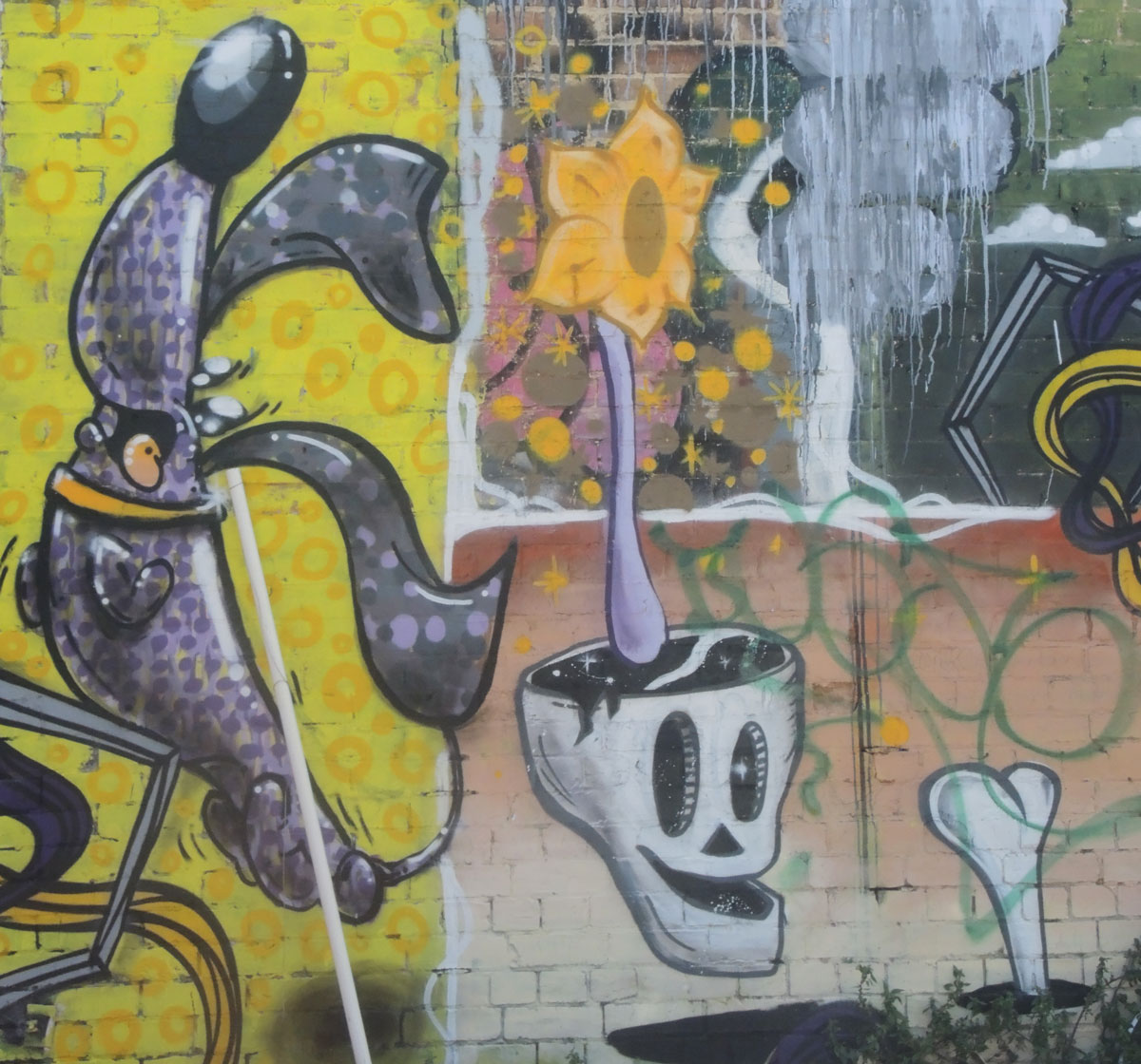 part of a larger mural with a skull, a bone in a hole and a sunflower growing out of the top of the skull