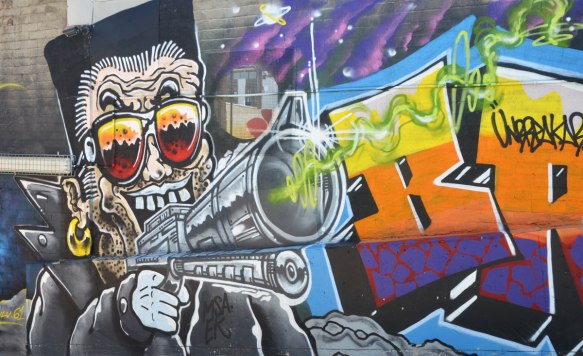 street art painting of a man holding a large gun pointing at the viewer
