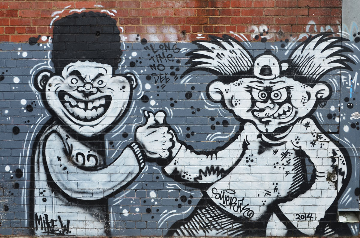 street art painting in grey tones of two guys meeting, thumbs together, both with silly grins on their faces. One has black afro hair and the other has long stick up in the air hair. 