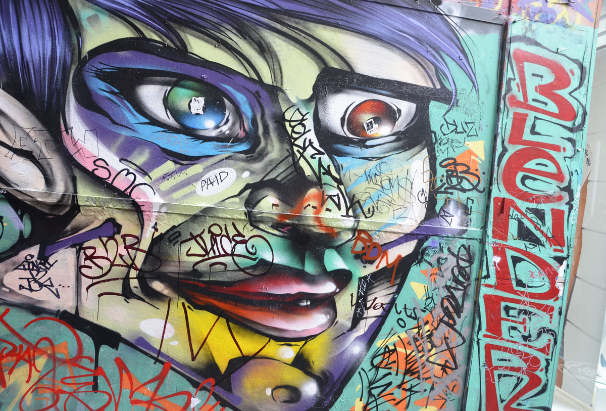 a multi coloured face painting in an alley that has had stickers added to it. The word beside the face is blender