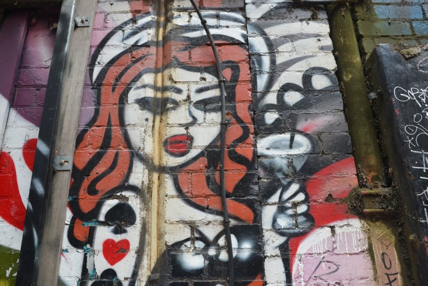 A woman with red hair and red lipstick is holding a martini glass. She has a club, spade and heart on her upper arm