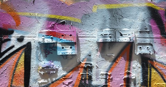 5 old cassette tapes are mounted on a wall and then covered with spray paint as part of a street art piece in Melbourne