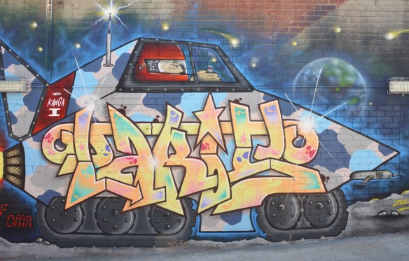 Street art painting of text within a large armed vehicle, large black tires