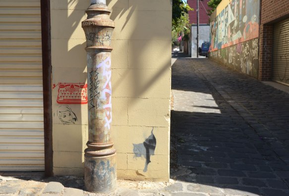 metal pole in front of a wall that has three small stencils on it, a red typewriter, a woman's face and a grey and black cat, in Bach Lane, an alley in Fitzroy