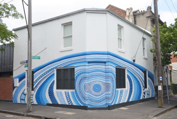 a building on a corner of an intersection, white, with concentric circles of blue patterns.