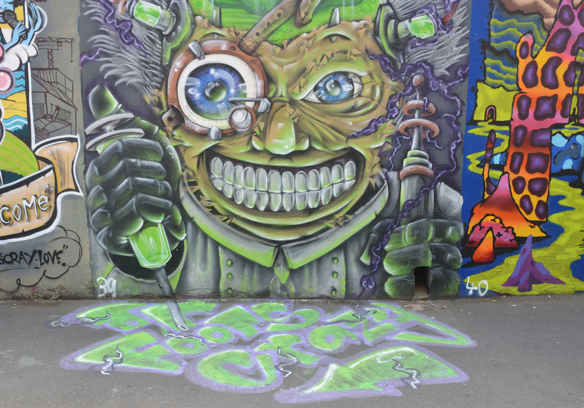 a green montrous face painted on a wall, with green paint flowing onto the pavement in front of it. 