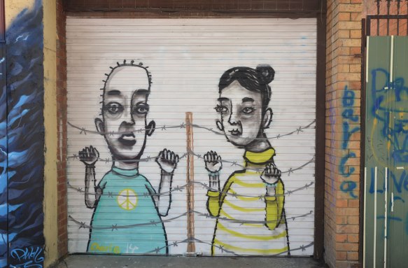 street art painting on a metal garage door of a couple standing behind a barbed wire fence