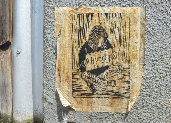 paste up of a drawing of a homeless man sitting on the sidewalk holding a sign that says hungry. printed on a book of postcodes 