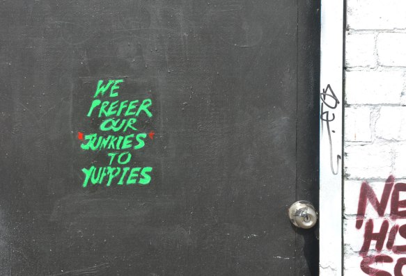 Green letters painted on a black door that say "We prefer our junkies to yuppies"