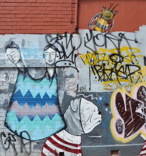 street art of a person with two heads wearing a long blue dress with no arms or legs visible but with one hand holding a very small person, also a large bumblebee street art painting. also a dog wearing a red and white striped top and a white dog face mask