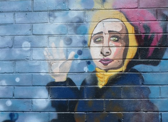 street art painting of a woman in a yellow head scarf and blue top waving 
