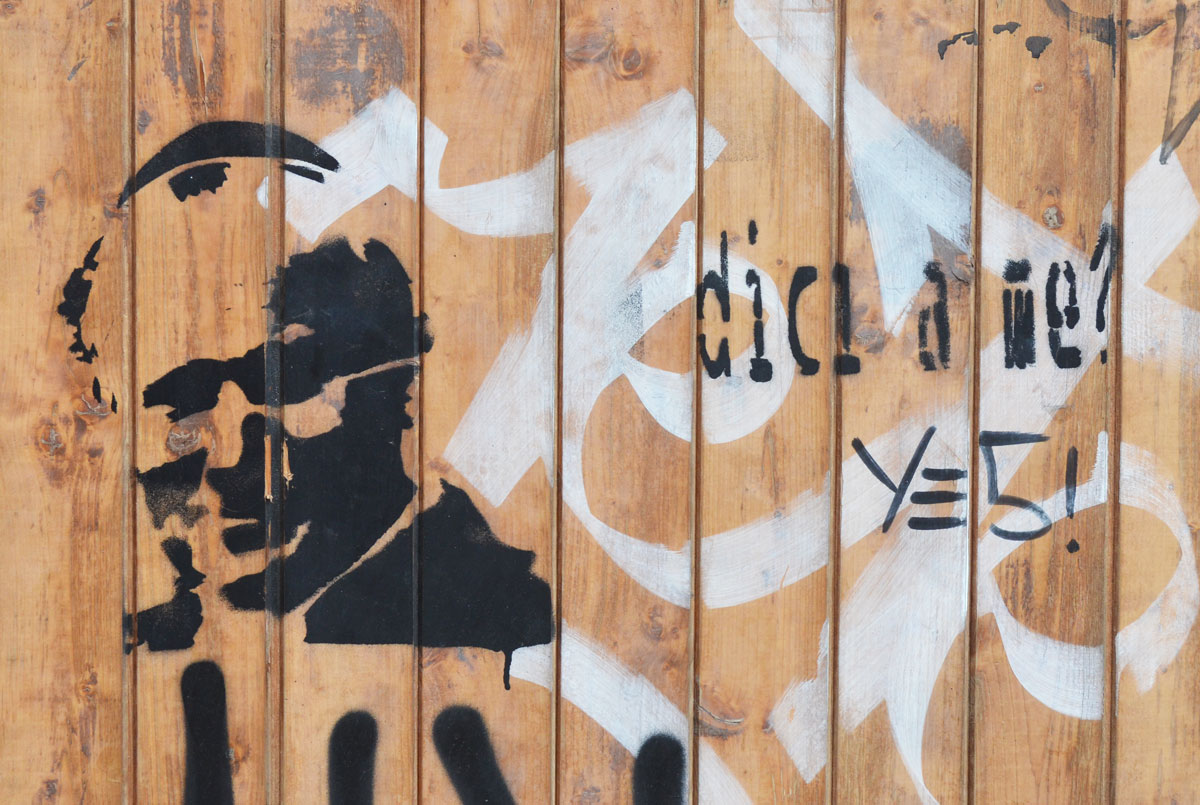 black stencil of the pope's head and shoulders on a brown wood wall. The words "dici a me" are stenciled on too. 