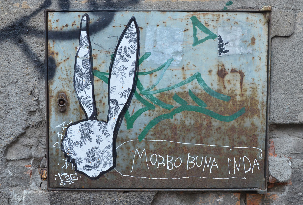 A silhouette shape of a rabbit's head and ears made of paper that has fern leaves on it. Pasted on a metal piece on a wall. 