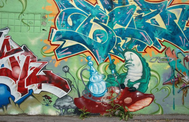 part of an Alice in Wonderland mural in a Montreal alley, looking down along the wall that the mural is on - a sleepy fat caterpillar sitting beside a large light blue hookah
