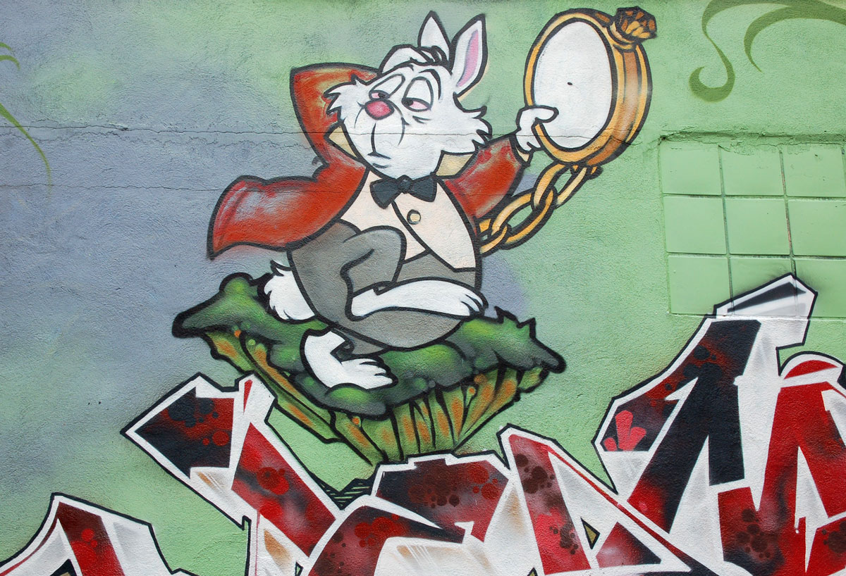 part of an Alice in Wonderland mural in a Montreal alley, looking down along the wall that the mural is on - an anxious looking white rabbit with a large pocket watch in his hand, wearing black bowtie 