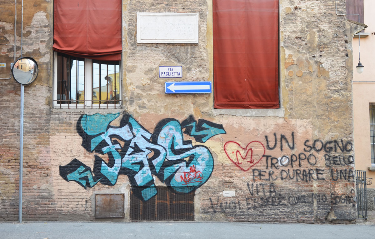 graffiti on an old stone building with burgundy coloured window shades, blue tag, other words written on the wall include 