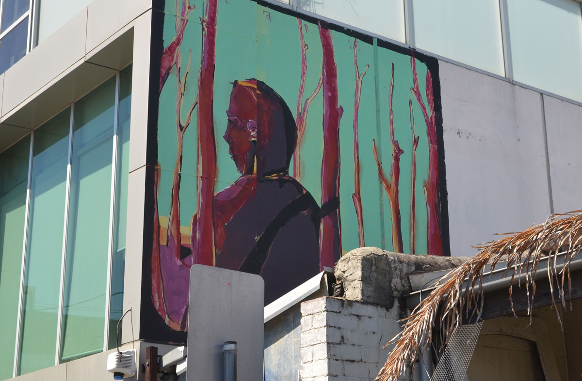 mural up high on the side of a building, a man amongst magenta trees.