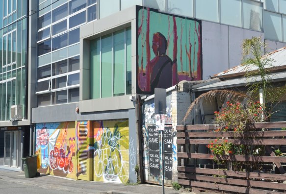 mural up high on the side of abuilding, a man amongst magenta trees. below it are two garage doors covered with graffiti