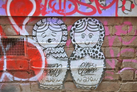 2 large paper paste ups of babushka doll shaped women. One with eyes open and smiling and the other with eyes closed.
