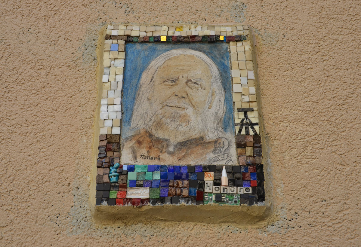small portrait of a man on a wall.  Hand drawn head and shoulder shot, framed with tiny pieces of mosaic tile - Honore
