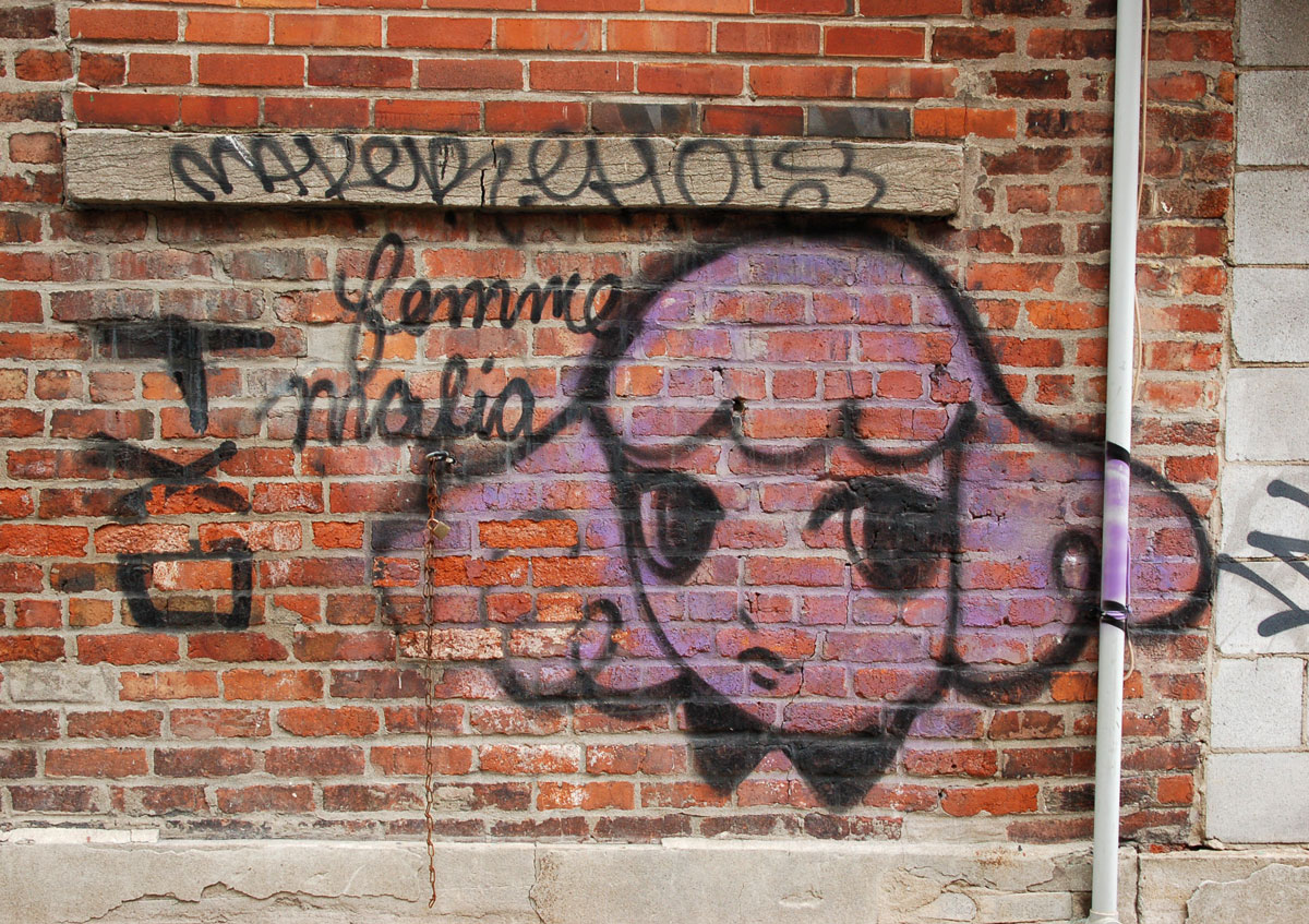 Starchild Stela character, a girl with shoulder length and slightly curly hair, painted in pink on a red brick wall with the words femme malia written in cursive beside it