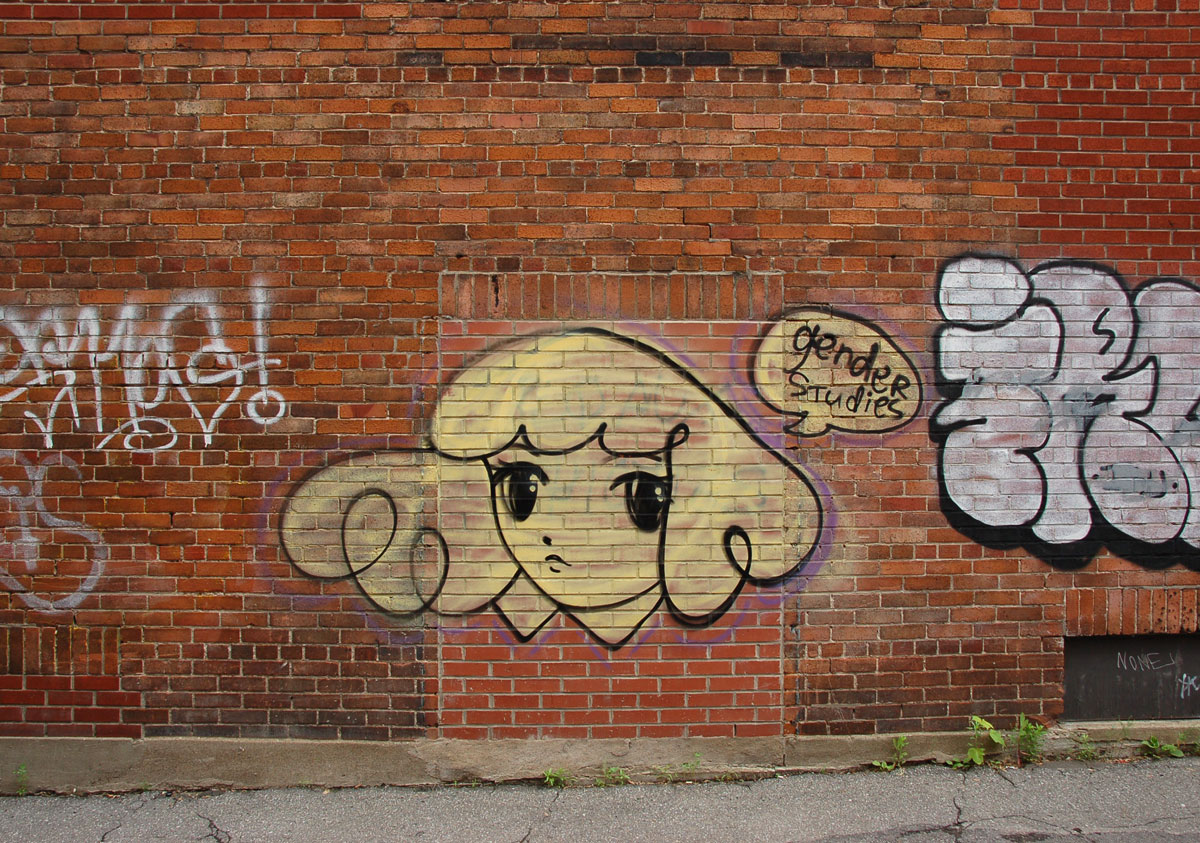 Starchild Stela character, a girl with shoulder length and slightly curly hair, in yellow on a red brick wall, with a word bubble that says gender studies
