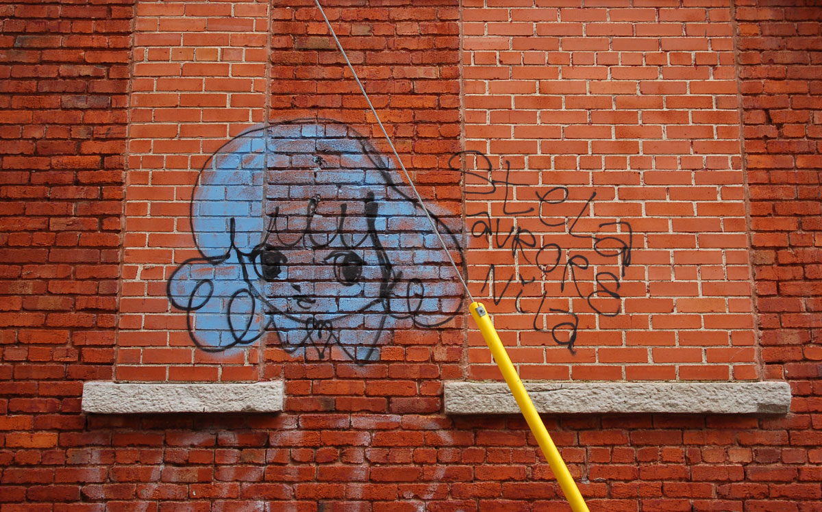 Starchild Stela character, a girl with shoulder length and slightly curly hair, large painting in blue on a red brick wall with the words Stela Aurure Nila scrawled in black beside it.