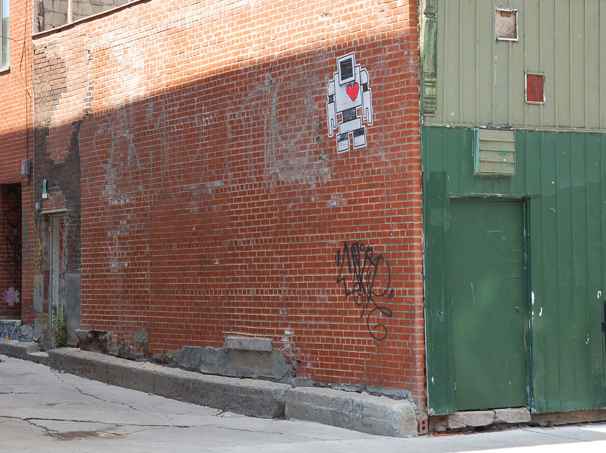 lovebot wheatpaste on a red brick wall on a building at the entrance to an alley