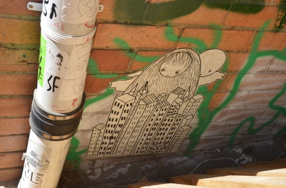 paste up of a black drawing on white, a girls head with very long hair looks over the top of a group of high rise buildings, cloud ans round sun behind her