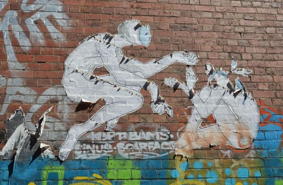fraying paste up (large) of two people in blank masks. One is seated. The other is reaching out to him or her, on a brick wall in an alley