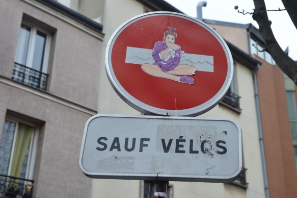 graffiti altered no entry sign, red circle with a white horizontal bar - added a pasteup of a woman sitting, wearing purple robe and slippers and holding a white stuffed bear 