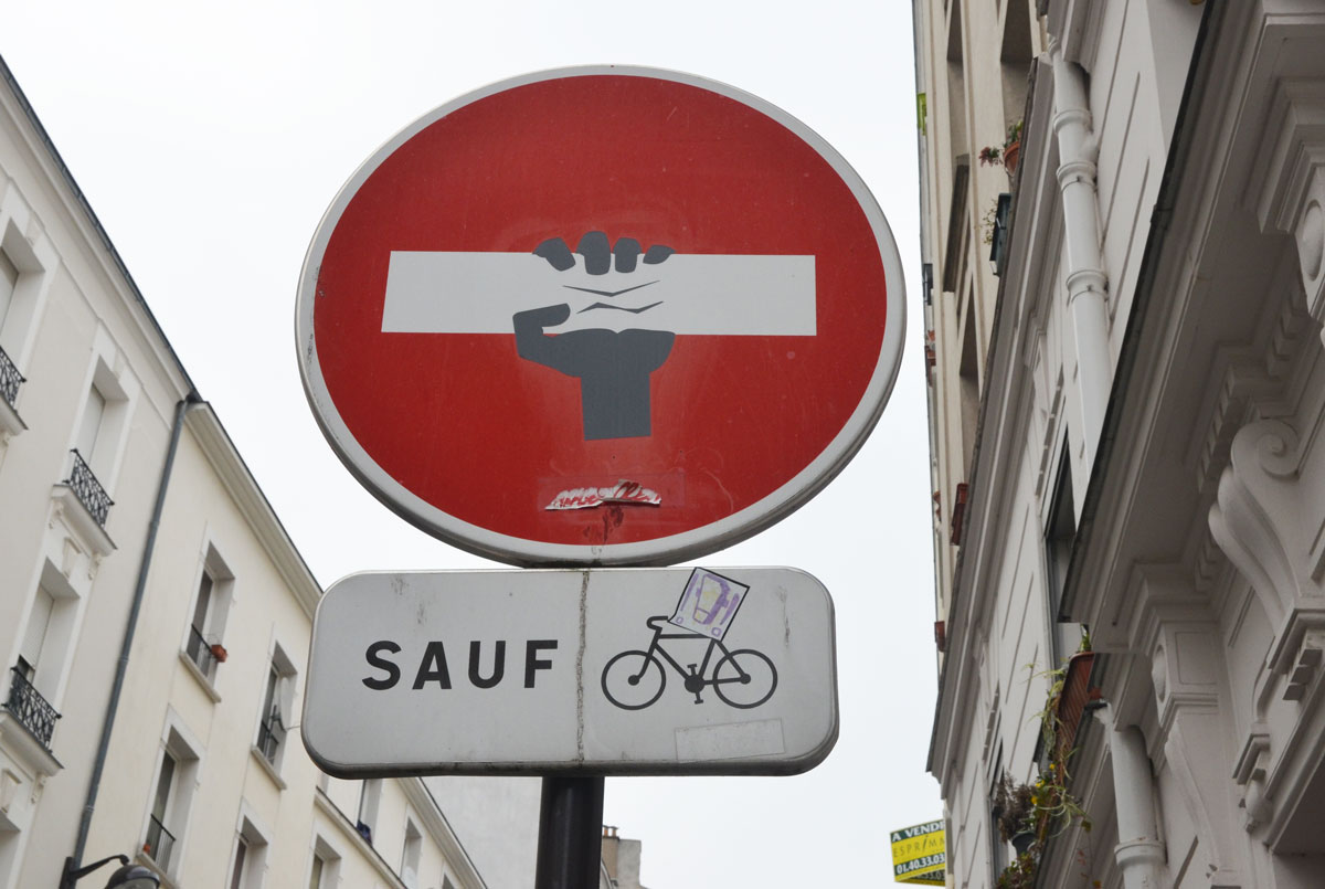 graffiti altered no entry sign, red circle with a white horizontal bar - added a black hand that looks like it's squeezing the middle of the bar