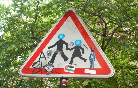graffiti altered triangular sign of two kids running while holding hands, blue circle stickers have been put over their heads