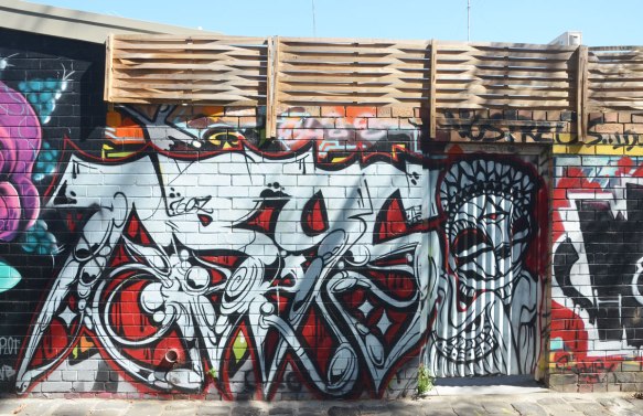 a large text street art piece in black, white and red, on a fence,
