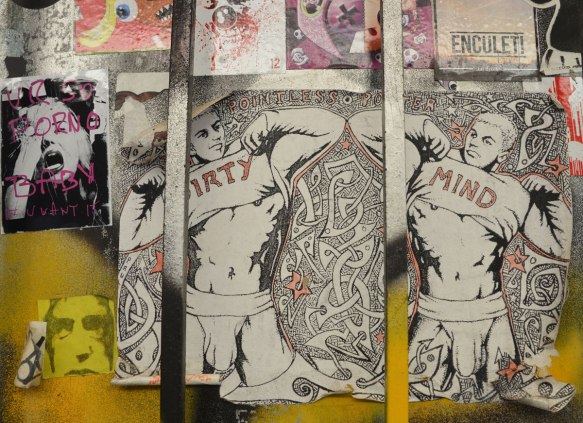 a group of pasteups on a wall. the largest one is of two guys in their underwear pulling their shirts up to reveal their stomachs and chest. One man has 'dirty' written on the shirt and the other has 'mind' written on his. 