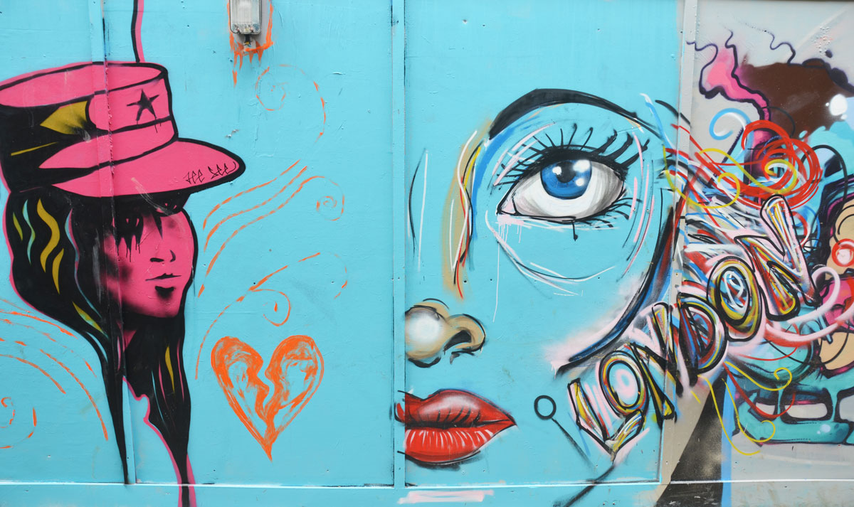 street art on construction hoardings on Blackall street in Hackney London. Light blue background. A young woman with hat all in dark pink, half of a woman's face (large) with bright red lips, blue eye and a multicoloured word London