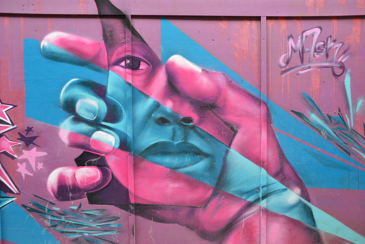 mural in pink and blue of a hand holding a face, by mask