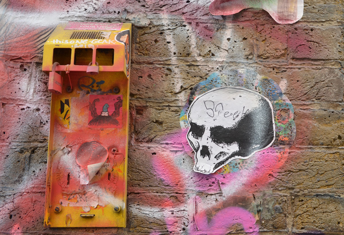 paste up of a skull, old mailbox broken, spray painted yellow and stickers on it