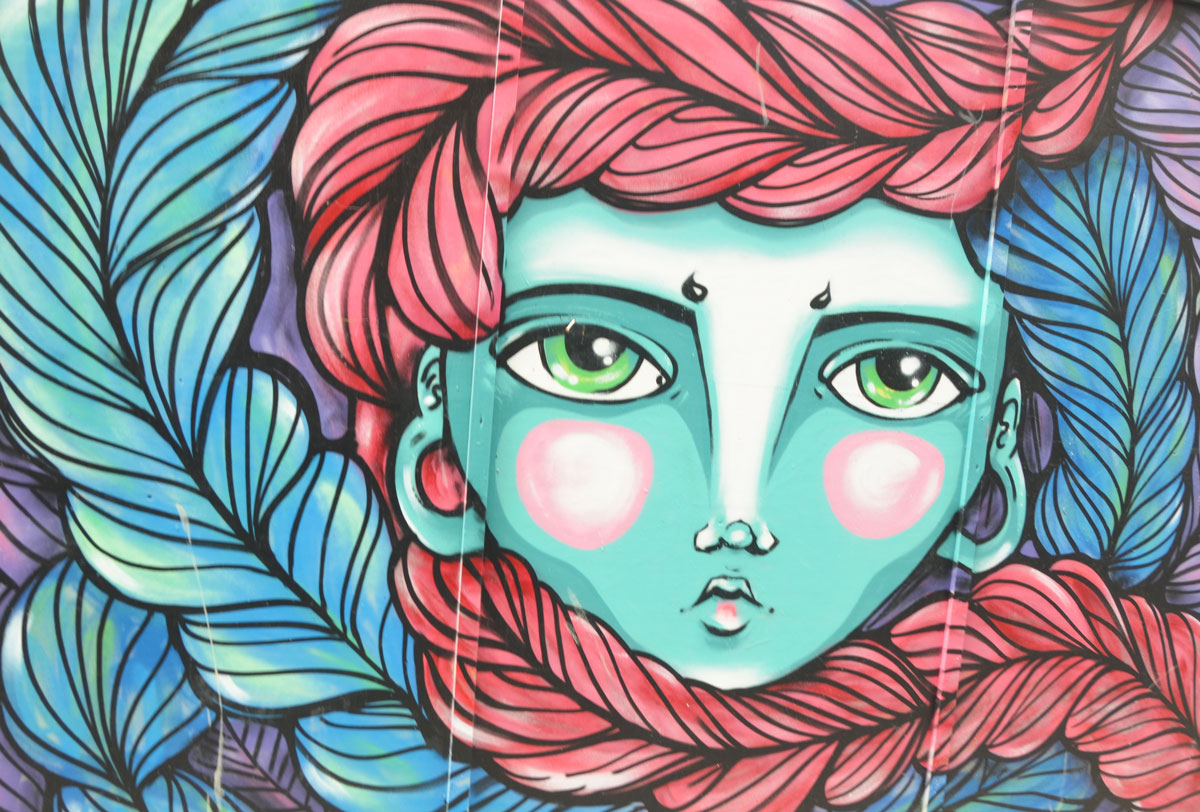 stylized painting of a woman's face, street art piece, with long braided hair wrapped around her face in red and blue