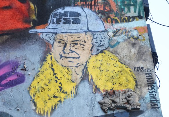 street art piece of head of Queen Elizabeth, wearing a hard hat with endless written on it, as well as a yellow scarf with Yves Saint Laurent logo on it. 
