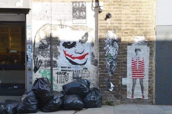 a wall in Fashion street, London E1, with a painting of the jokers face and some paste ups 