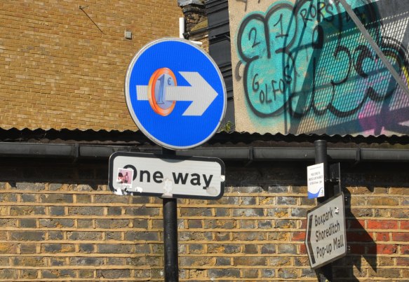 one way sign, blue circle with an arrow pointing left, aone euro coin has been added to make the arrow look like it has pierced the coin