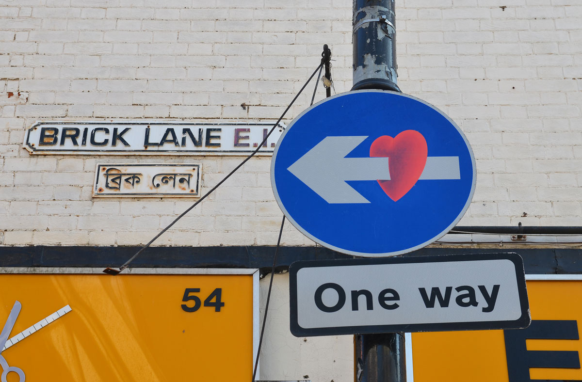 one way sign, blue circle with an arrow pointing left, a heart has been added to make the arrow look like it has pierced the heart 