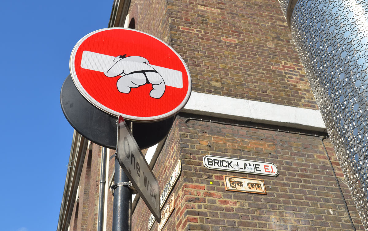 altered red and white no entry street sign , backside of a Japanese suomo wrestler trying to lick up the white bar 